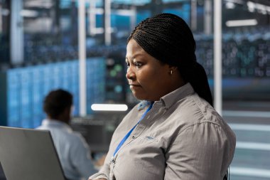 Engineer using notebook device to oversee data center machines processing workloads. African american woman doing maintenance on server rigs tasked with solving complex operations