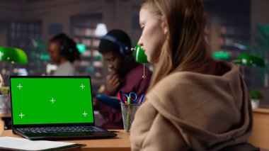 Üniversite öğrencisi yeşil ekranın yanına proje fikirleri yazarak güvenilir kitaplardan ve kütüphanedeki diğer kaynaklardan alıntılar topluyor. Eğitici materyallere danışmanlık yapan bir kız. Kamera B.