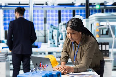 Modern industry expert examines production data in a solar tech facility, ensuring innovation, efficiency and professional oversight to drive renewable energy success. Sustainable solutions.