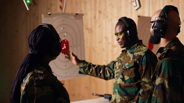 Portrait of joyous army soldiers wearing safety gear in shooting gallery, preparing to fire at targets. Smiling military units in uniform and protection equipment testing accuracy, camera B