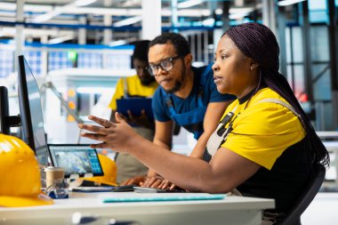 African american workers checking up on manufacturing equipment in solar panel factory, reading documentation files. Team of engineers in industrial facility inspecting production process.