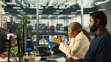 Supervisor in office discussing with employee about key performance indicators for revenue, profitability and operational efficiency. African american manager supervising employee at work, camera B