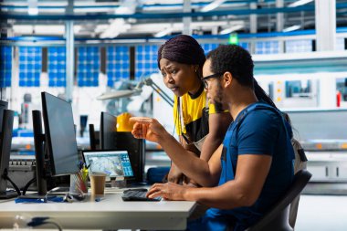 Photovoltaics tesis ekibi güneş panellerini elle inceledi, bilgisayar programındaki performansı izledi. Siyah yöneticiler robotik silah mekanizması parametrelerini okuyor.