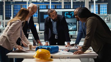 Fabrika yönetimi şemaları inceliyor, üretimi genişletmek için birlikte çalışıyorlar. Endüstriyel fabrika yöneticileri beyin fırtınası yapıyor, tesisin planı üzerinde tartışıyorlar, kamera A