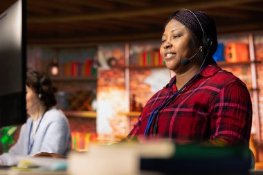 Gülümseyen çağrı merkezi çalışanı, donanım sorunuyla ilgili teknik sorulara cevap vermek için kulaklıkla mikrofon kullanıyor. Müşteri destek işini yapan mutlu kadın, sorunları çözmek için bilgisayarı kullanıyor.