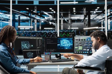 Tekerlekli sandalyedeki veri merkezi mühendisi ve iş arkadaşı otomatik görevleri denetlemek için yapay zekayı kullanıyor. Kapsayıcı sunucu çiftliğinde engelli işçiler ve analitiğe dayalı iş arkadaşı modifikasyon sistemleri