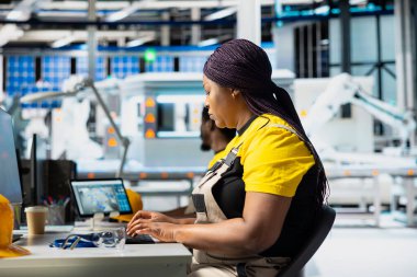 Mühendis güneş paneli yenilenebilir enerji konfigürasyonlarını inceleyerek güneş pillerinin üretim hattı üzerinde çalışıyor. Afrika kökenli Amerikalı kadın işçiler CAD endüstriyel yazılımı kullanıyor.