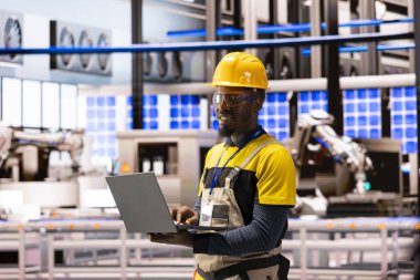 Akıllı üretim tesisindeki erkek mühendis robot kolu optimize ediyor ve otomatik üretim hattını koruyor. Endüstri 4.0 uzmanlığı yüksek teknoloji endüstriyel santralinde yenilenebilir enerji donanımı üretiyor.