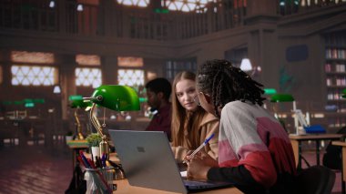 Üniversite öğrencisi kampüs kütüphanesinde bir arkadaşıyla el yazısı notlarını tamamlamak için sınav hazırlığı yapıyor. Veritabanından bilgi paylaşan kızlar. Kamera B.