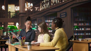 İlkokul öğrencileri bir profesörle birlikte çalışıp sınıf ödevleri için alıştırma yapıyorlar, çalışma masasında öğrenme becerileri geliştiriyorlar. Öğretmen kızlara müfredat malzemelerini açıklıyor. Kamera A.