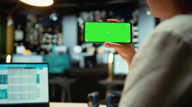 İş kadını, geç saatlere kadar çalıştığı sırada cep telefonuyla yeşil ekrana bakıyor. İş yerindeki mesai saatlerinden sonra yönetici görevlerini tamamlıyor. İzole kopyalama alanı kullanılıyor. Kamera A.