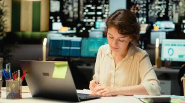 İş kadını, bilgisayar ekranından önemli fikirleri kağıda döküyor, gece geç saatlerde görevleri planlıyor ve programlıyor. Hedefleri yansıtan sunum için el yazısıyla not almak. Kamera B.