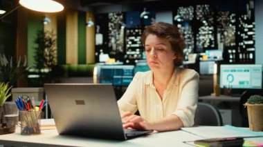 Yönetici iç geçiriyor, saatler sonra gergin ve bunalmış hissediyor, yorgunluk belirtilerine rağmen sınırları zorluyor. İş yerindeki zorluklar, yorgunluk ve cesaretsizlik rahatsızlık veriyor. Kamera A.