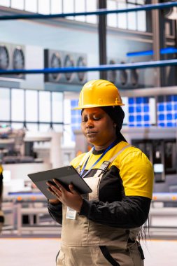 Yüksek teknolojili imalat mühendisi, tabletteki yazılımla robot iş akışları geliştiriyor. Afro-Amerikan otomasyon uzmanları dijital arayüzle endüstriyel fabrika makinelerini izleyip geliştirdiler.