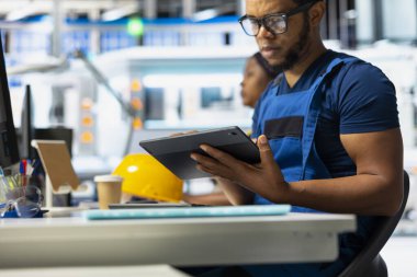 Güneş paneli tesisindeki siyah teknisyen tabletteki fotovoltaik sistem performansını inceliyor. Endüstriyel üretim tesisinde verimliliği optimize etmek için üretim hattını analiz eden erkek çalışan.