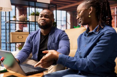 Bir iş fikri üzerinde işbirliği yapmak için kanepeye oturan Afrikalı Amerikalılar, modern teknoloji ve araçları trendleri analiz etmek ve başarıyı artırmak için kullanıyorlar. Bağımsızlar iş akışını verimli bir şekilde geliştiriyor.