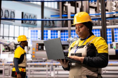 Afrikalı Amerikalı teknisyen otomatikleştirilmiş taşıma bantları ve endüstriyel fabrikada robot kollarında bakım yapıyor. Endüstri 4.0 uzmanı akıllı fabrika ve optimal performansın verimli çalışmasını garanti ediyor.