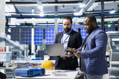 Çeşitli mühendisler ve teknisyenler, yenilenebilir enerji üretimi ve sürdürülebilir yenilikleri geliştirmek için fikirlerini paylaşmak üzere bir güneş paneli fabrikasında işbirliği yapmaktadırlar..