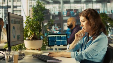 Ofisteki işçiler çizelgeleri incelerken sabit telefon kullanarak müşterilerle konuşuyorlar. İşte çalışan iş ortağıyla çağrı sırasında tartışıyor, iş performans ölçümlerini analiz ediyor, kamera B