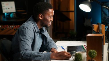 Serbest çalışan siyahi adam, evde birden fazla iş yapıyor. El yazısı notlar alıyor ve internette araştırma yapıyor. Verimliliği arttırmak için bir planlayıcının programını ve görevlerini yönetmek. Kamera B.