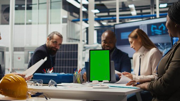 Менеджеры в офисе рассматривают отчеты о солнечных технологиях на изолированных планшетах. Акционеры, использующие хроматический ключ, обсуждают инвестиционные возможности в производство зеленой энергии, камера А