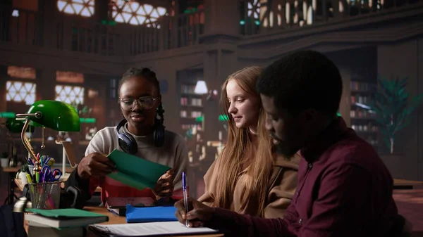 Çok kültürlü öğrenci grubu, kütüphanede notları olan dizüstü bilgisayar ve ders kitaplarını kullanarak bir üniversite dersi için finans projesini tartışıyor. Girişimcilik ve yönetim becerileri. Kamera B.