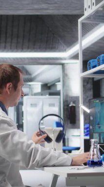 Dikey Görüntü Bilimadamı, bir bilim laboratuvarında deney yaparken, kulaklık takarak ve moleküler biyoloji veya biyoteknoloji araştırmalarını uyumsuzlukla harmanlayarak müzik dinliyor.