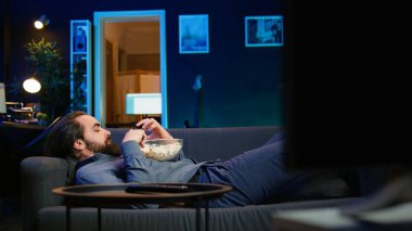 Adam evde oyalanıyor, kanepeye uzanıyor, abur cubur yiyor, televizyon seyrediyor. Sıkıcı bir yaşam tarzı, kanepede uzanmak, televizyon izleyerek zaman harcamak, patlamış mısır yemek, kamera B