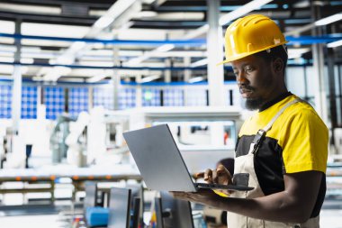 Güneş paneli fabrikasında bilgisayar verileri üreten teknisyen gözlemcileri, verimli güneş enerjisi üretimini desteklemek için çalışan ince unes ekipman ayarları. Montaj hattının yanında oturan adam.