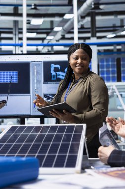 Fabrika yönetimi yöneticisi yatırımcılara güneş pili materyalleri sunuyor, fon sağlıyor. Afrikalı Amerikalı iş kadını, sunum sırasında sanayi tesisi varlıklarını hissedarlara gösteriyor