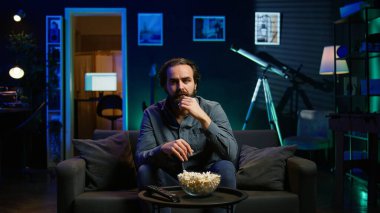 Tembel kanepe patatesi insanı düşüncesizce TV 'de programlar izliyor ve patlamış mısır yiyor, ekrana yakından bakıyor. Oturan adam abur cubur yerken akılsız eğlence tüketiyor, kamera B