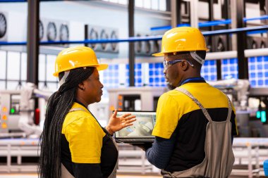 Yüksek teknoloji üretim tesisinde otomatikleştirilmiş üretim hattını denetleyen siyahi endüstriyel profesyoneller. Afro-Amerikan endüstrisi 4.0 uzmanları akıllı fabrika optimizasyonu için dijital arayüz kullanıyorlar.