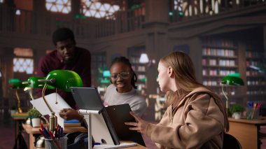 Öğrenci üniversite kütüphanesinde sınıf arkadaşlarıyla el yazısı notlarını tamamlamak için sınav hazırlıkları yapıyor. Akademik takdirnameler için bilgi toplayan bir kız. Kamera B.
