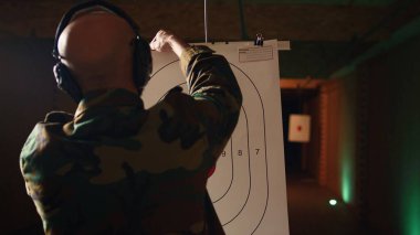 Atış poligonunda, işitmeyi engellemek için kulaklık takan bir adam silahla hedefleri vuruyor. Silah eğitimi, boğa güreşi, silah seslerinden zarar görmemek için güvenlik teçhizatı, kamera A.