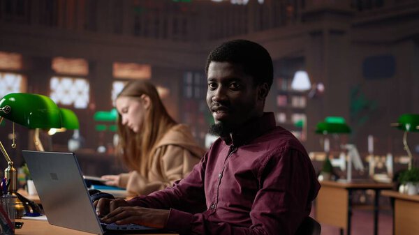 Black male student collecting academic information from the campus library, doing research to help with exam preparations. Pupil with education opportunity fights for a certificate. Camera A.