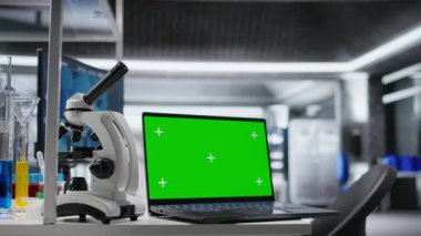 Bilgisayarlı dizüstü bilgisayar boş laboratuarda, araştırma araçları, kan örnekleri ve kavanozlarla birlikte. Klinik kurulum biyoteknolojiyi ve test için kimya ekipmanlarını yansıtıyor.