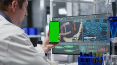 Biolab masasında laboratuvar teknisyeni olan kimya uzmanlarının kullandığı akıllı telefon ekranında genetik araştırmalar, nanoteknoloji ve tıbbi keşif ve yenilik için veriler üzerinde duruyoruz. Kamera B.