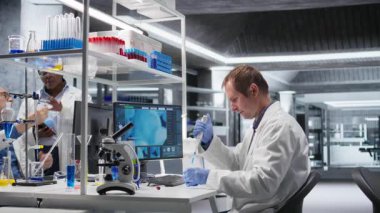 Erkek bilim adamı, laboratuarda işlem sırasında pipeti kavanozun üzerine damlatarak tutar. Genetik araştırmaları, nanoteknoloji ve çözümleri analitik yöntemlerle destekleyen karışım hazırlığı. Kamera A.