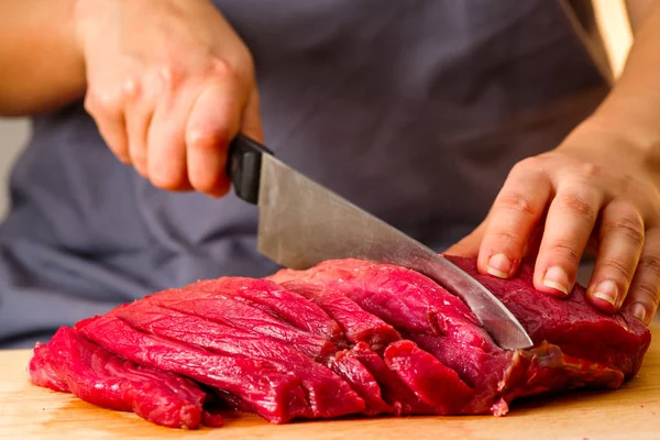 Mulher corta carne fresca na cozinha — Fotografia de Stock