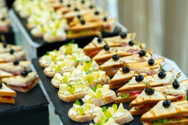 Canapés con queso y uvas y sándwiches con tocino y col y tomates con aceitunas en un pincho sobre una mesa buffet —  Fotos de Stock