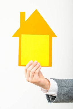 Elinde sarı-turuncu karton bir ev olan bir çocuğun eli.