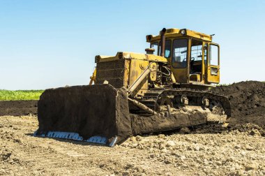 Sarı buldozer traktörü tarlada duruyor.