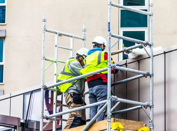 2015年6月9日 两名建筑工人 穿着黄色安全夹克和头盔之间的脚手架在建筑工地上 — 图库照片
