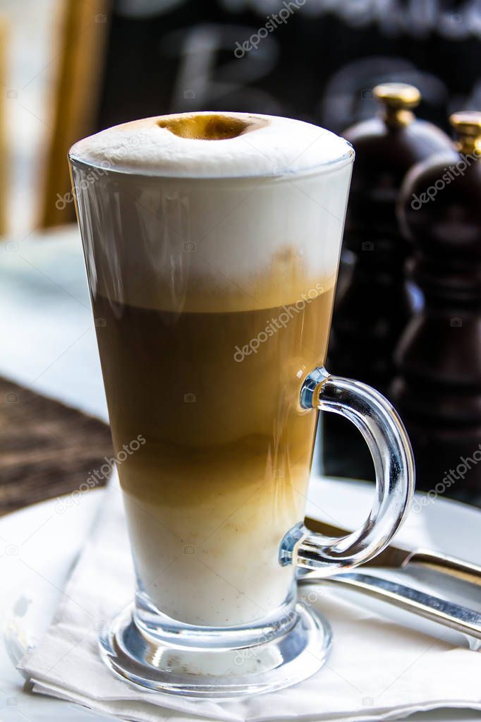 Hot latte macchiato coffee with tasty foam and cinnamon in tall clear glass on serving table