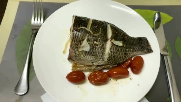 フォークとナイフで赤ナプキンの白いプレート上に玉ねぎとトマトで聖ピーターの魚を焼き 野菜とティラピアロースト — ストック動画
