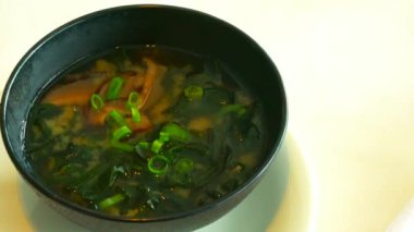 Büyük siyah kasede Miso çorbası. Geleneksel Japon yemeğidir. Ana malzemeler miso macunu, tofu, wakame deniz yosunu ve shiitake mantarlarıdır. 4K
