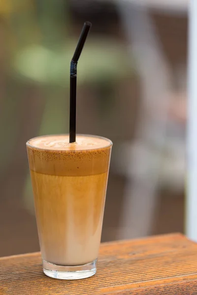Iced coffee in a glass with straw. Frappe coffee isolated on a wooden table.