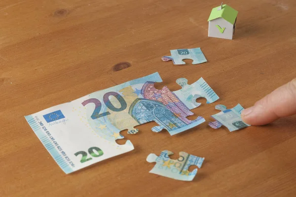 Hand putting a piece on a 20 euro puzzle: saving to buy a house concept
