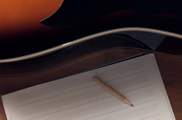 写歌的概念 一个空白的乐谱和一支铅笔放在一个木桌上 旁边是一把音响吉他 — 图库照片