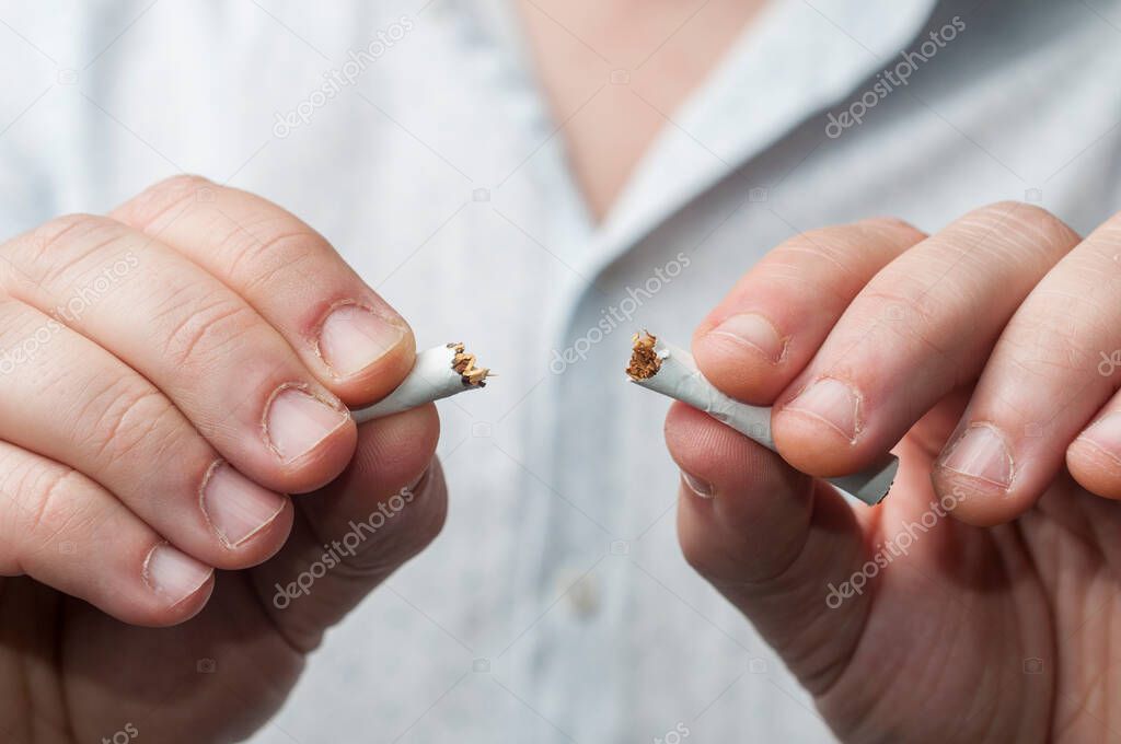 Quit smoking concept: man in shirt breaks a cigarette in two
